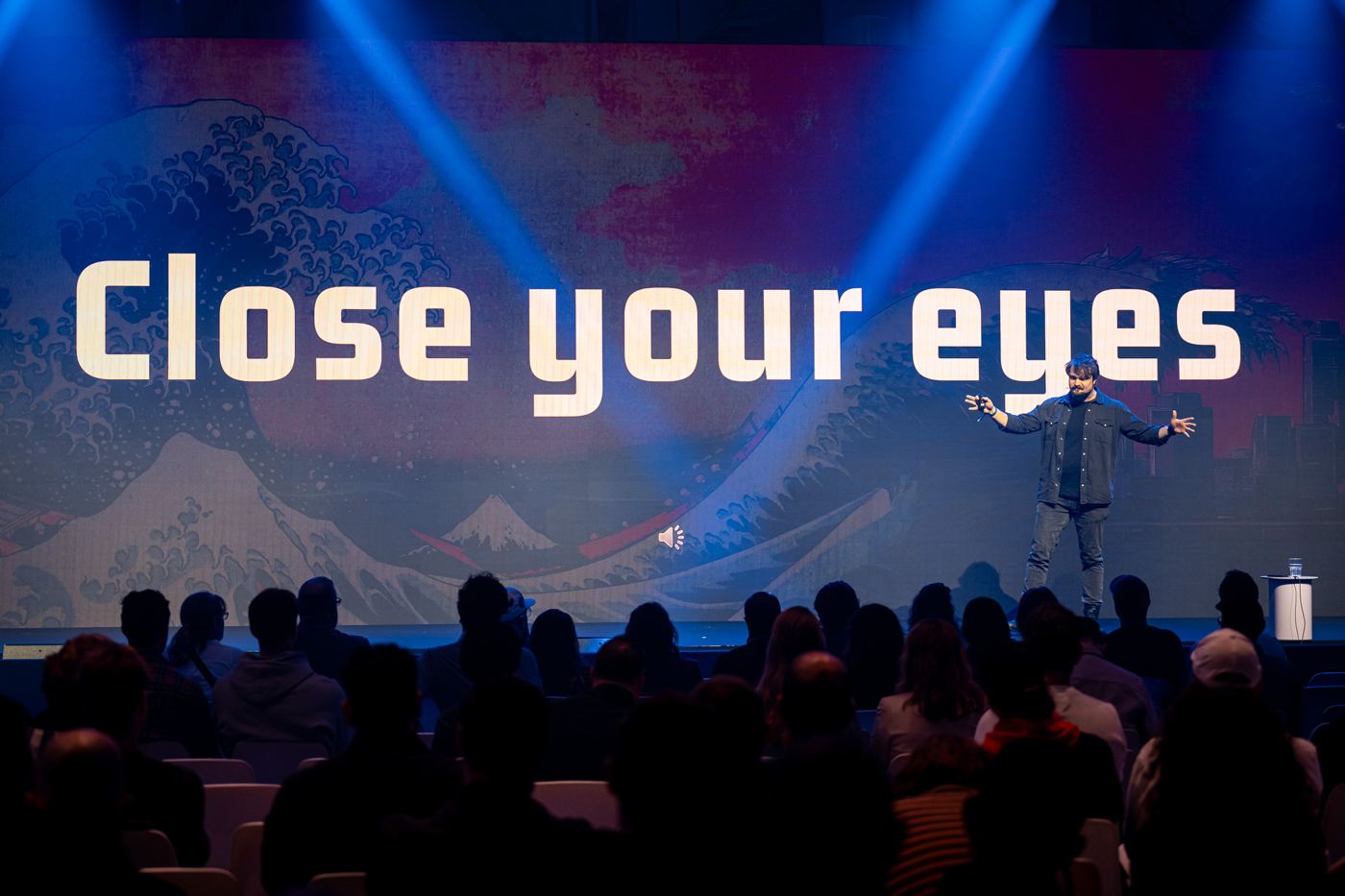 Een verduisterde zaal, het grote scherm zegt: Close your eyes
